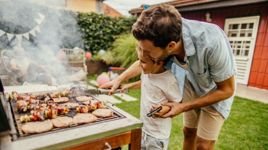 A man is grilling meat in outdoor with his boy
