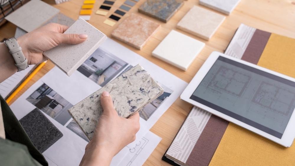 Hands of young female designer holding two samples of marble tile over table