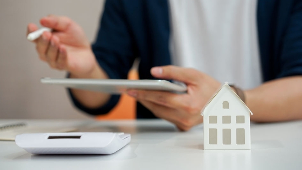 Close up of a house model with realtors holding tablet and explaining to customer about