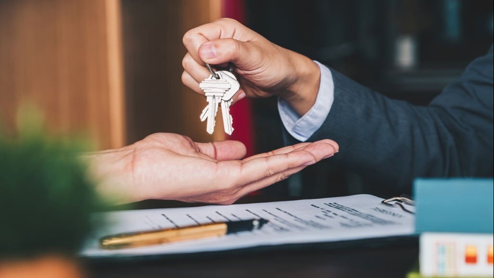 Real estate agent giving house keys to new owner and signed agreement in office