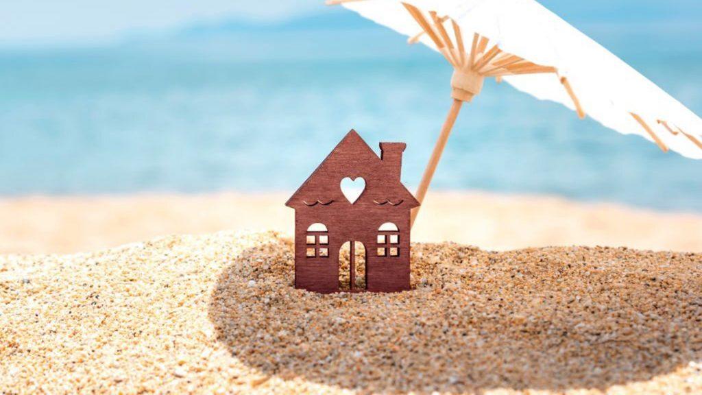 Miniature house and umbrella on beach blue sea and sky