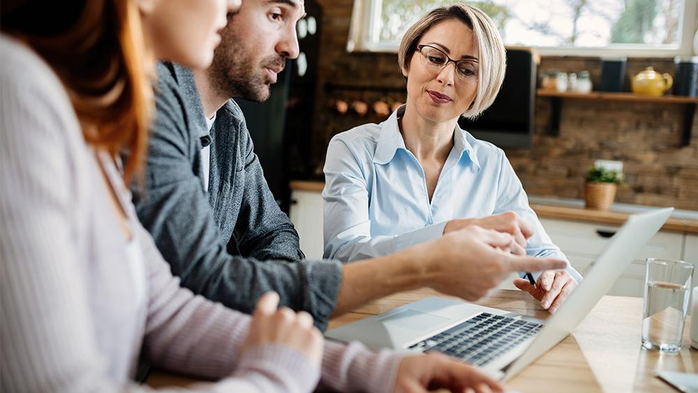 Smiling real estate agent young couple using laptop during meeting