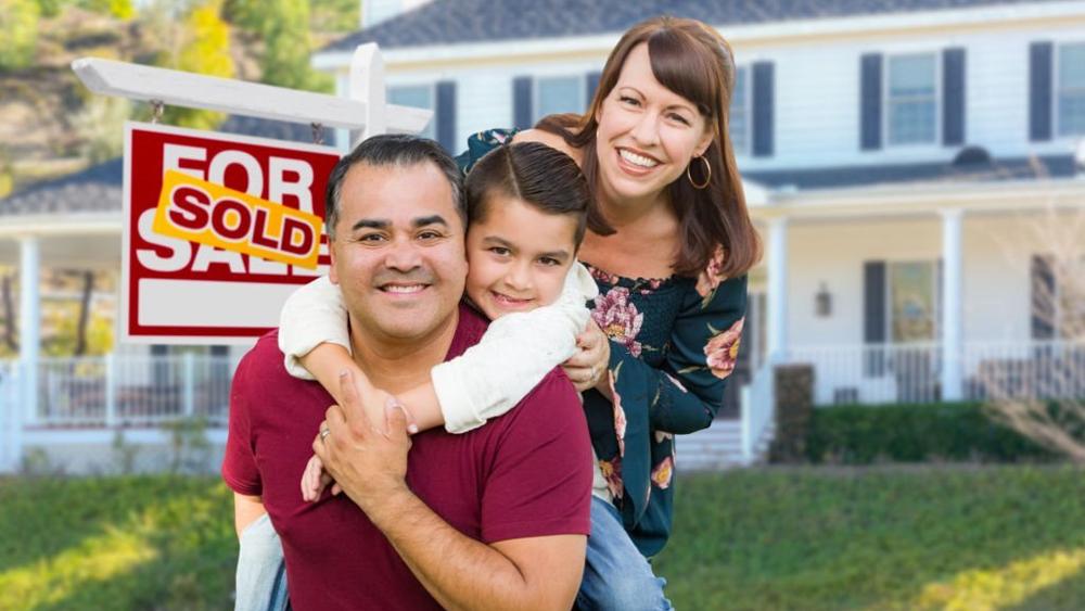 Happy family in front of house and sold for sale real estate sign