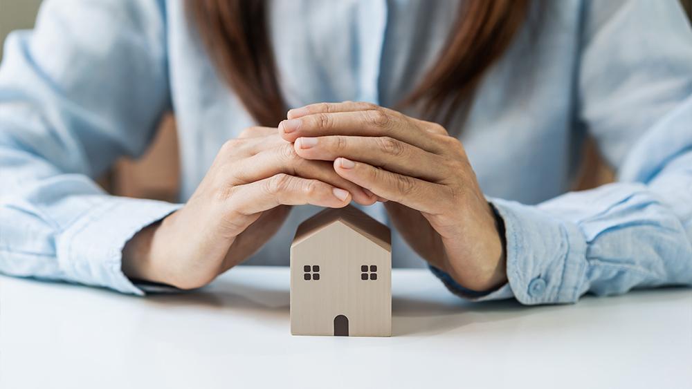 Young woman hands protecting miniature house home