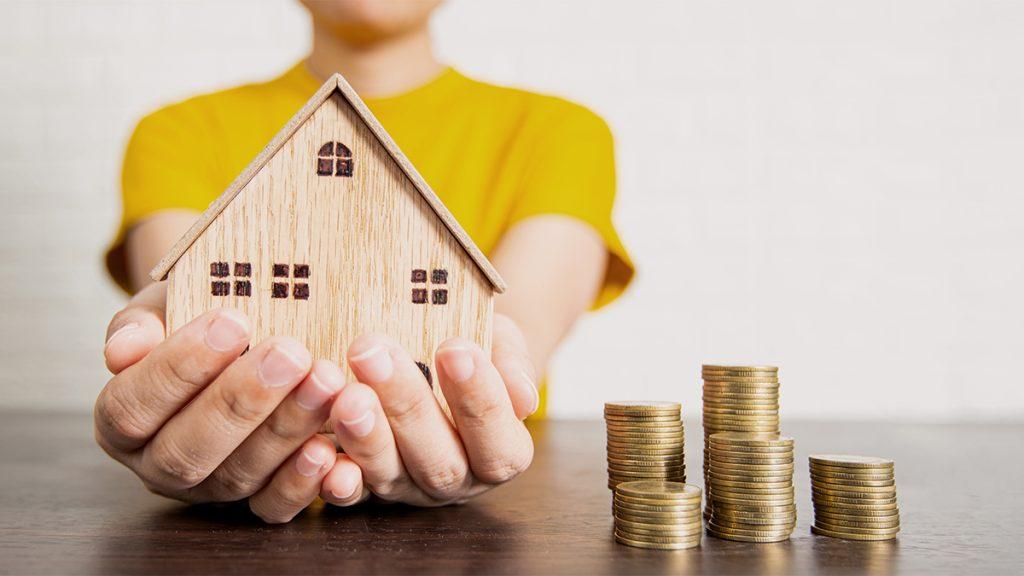 Real estate woman holding wooden house model and money on table