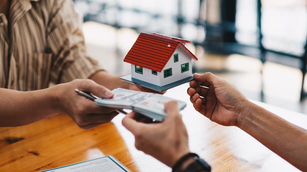 Closeup of hands giving house model to other hand