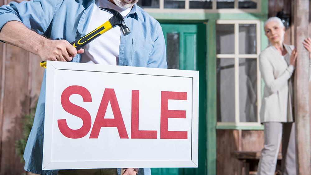 An elderly couple installing sale sign to sell their house