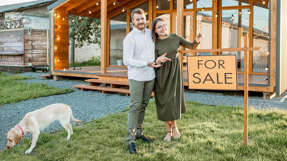 Couple standing next to the for sale sign to sell their country house