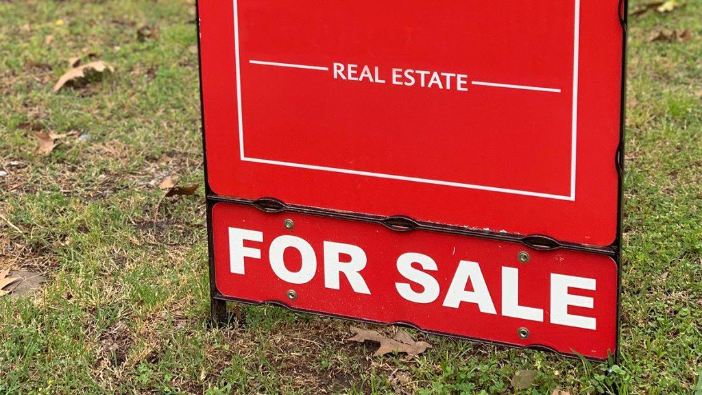 Red real estate for sale sign at a neighborhood