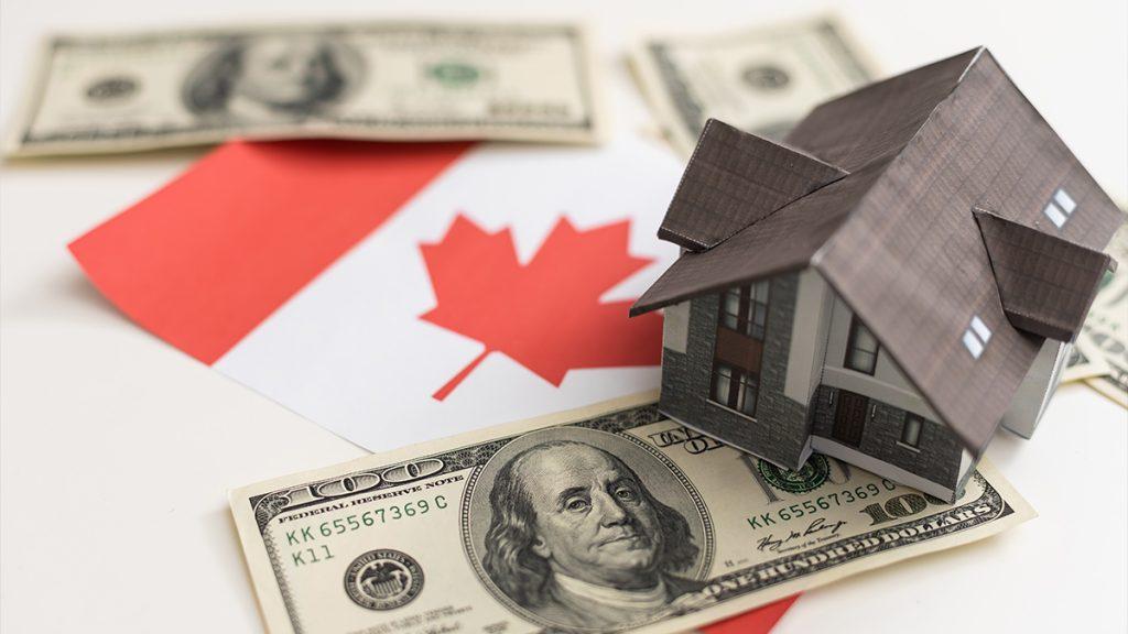 Cash dollars next to a wooden house model located on the Canada's flag with the paying in cash for buying a home concept